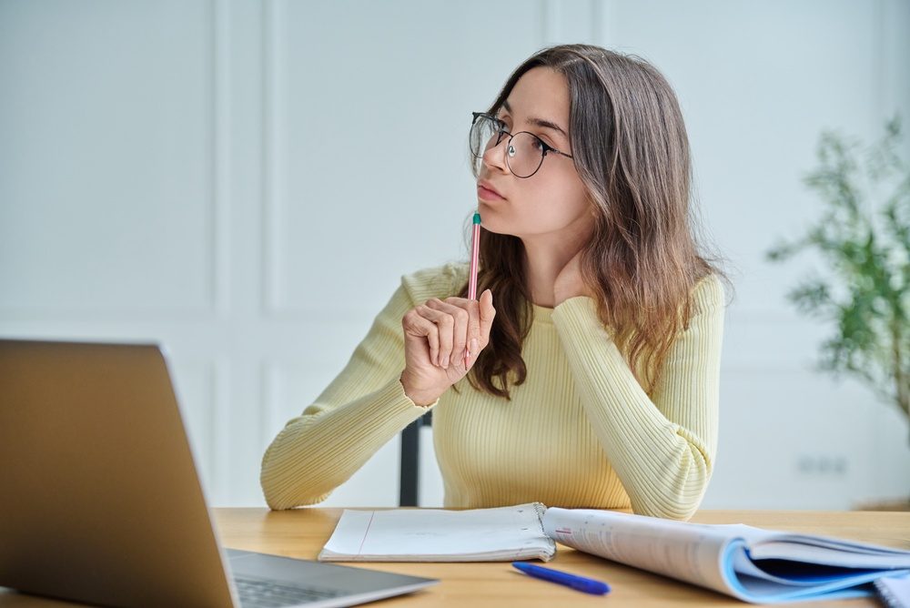 Schülerin denkt beim Lernen am Laptop nach